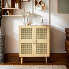 a wooden cabinet sitting on top of a hard wood floor next to a vase with flowers