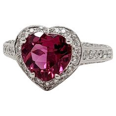 a heart shaped pink tourmaline ring with diamonds on the sides and an intricate band around it