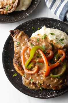 two black plates topped with meat covered in gravy and veggies next to mashed potatoes