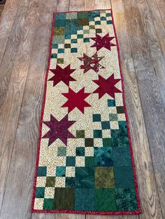 a quilted table runner with red and green stars on the top, sitting on a wooden floor