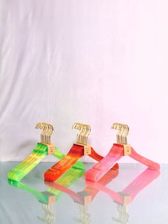 three plastic clothes hangers sitting next to each other on a reflective surface with white background