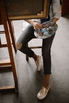 a woman sitting on top of a wooden chair holding a purse in her hand and looking at the camera