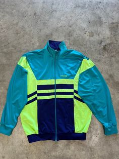 Vintage 90s neon blue Adidas track jacket in great vintage condition. Size: L(M) (see measurements) Measurements: - Chest (armpit to armpit: 72 cm (28.3") - Length from the backside (Center bottom of the collar to center bottom of the garment): 80 cm (31.5") - Sleeve (COLLAR seam to end of arm cuff): 87 cm (34.2") NOTE: Due to the age, clothing/items can shrink or it may be that the sizing from that time the item was made in, is not the same as the sizing in modern clothing and current sizes. Ma 90s Style Blue Nylon Track Jacket, Retro Color Block Long Sleeve Track Jacket, Vintage Multicolor Winter Track Jacket, Vintage Blue Nylon Track Jacket, Vintage Long-sleeve Nylon Track Jacket, Adidas Windbreaker, Adidas Track Jacket, Adidas Vintage, Color Block Jacket