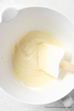 a white bowl filled with batter and butter on top of a wooden spatula next to a spoon