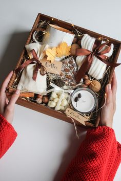 a person holding a box filled with different types of food and candles on top of a table