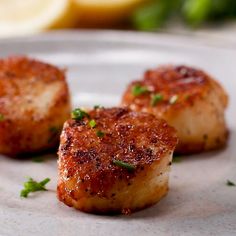 three seared scallops on a plate with lemon wedges in the background