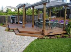 a wooden deck with chairs and table next to a brick walkway in a backyard area