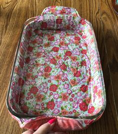 a person holding a pink flowered suitcase on a wooden table next to a cup