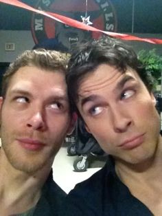 two men posing for the camera in front of a red ribbon