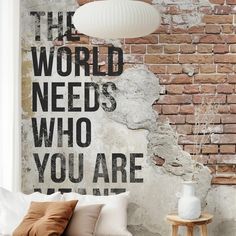 a bedroom with brick wall and white bedding in front of a large poster that says the world needs who you are