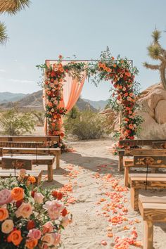 an outdoor ceremony setup with orange flowers and greenery on the aisle, surrounded by wooden benches