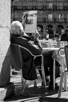 an older man sitting at a table reading a newspaper