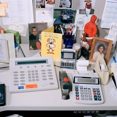 a cluttered desk with an old calculator, cell phone and pictures on it