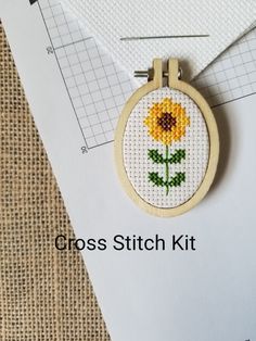 a cross stitch sunflower is hanging on a piece of paper next to some scissors