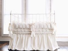 a white crib with ruffled bedding in front of a window and wooden floor