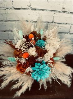 an arrangement of flowers and feathers on a wooden table in front of a brick wall