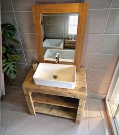 a bathroom sink sitting under a mirror next to a wooden stand with a potted plant