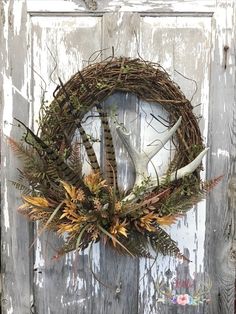 a wreath with antlers and plants hanging on the front door to an old wooden door