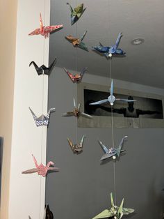 several origami birds hanging from strings on the wall in front of a mirror