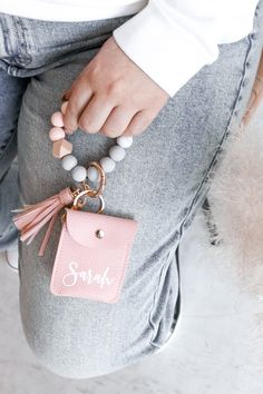 a person holding a pink bag with a tassel on it's wrist and a small keychain