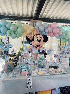 a table topped with lots of cake and balloons next to a minnie mouse balloon arch