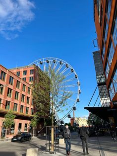 two people walking down the street in front of a ferris wheel on a sunny day