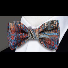 Brown, Red, Orange, Light Blue Paisley Self-Tie Bow Tie Picture yourself wearing a luxurious paisley silk bow tie and accenting silk pocket square, crafted from the finest materials and bursting with rich, vibrant colors. The intricate paisley pattern features shades of brown, red, orange, and light blue, creating a mesmerizing effect that draws the eye and exudes a sense of sophistication and style. To showcase this stunning bow tie, pair it with a crisp white or light blue dress shirt. The con Elegant Multicolor Bow Tie, Elegant Red Bow With Butterfly Knot, Elegant Fitted Multicolor Bow Tie, Elegant Multicolor Paisley Print Suit And Tie Accessories, Elegant Multicolor Paisley Print Ties, Orange And Light Blue, Clean Background, Charcoal Gray Suit, Light Blue Dress Shirt