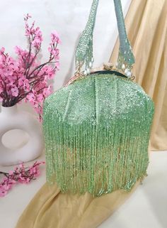 a green purse sitting on top of a table next to a vase with pink flowers