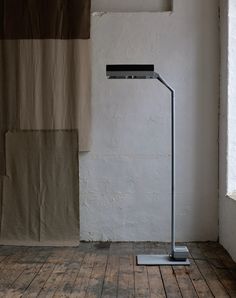 a floor lamp in front of a white wall and wooden floor with curtains behind it