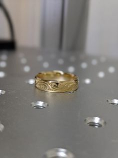 a gold wedding ring sitting on top of a metal surface with lots of small white dots