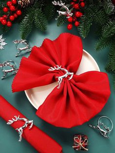 red napkins and silver rings are on a plate next to christmas decorations, such as pine branches