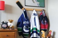 several sports jerseys hanging on the wall next to a dresser with stuffed animals and an alarm clock