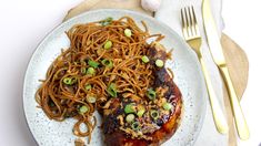 a white plate topped with meat and noodles on top of a wooden table next to silverware