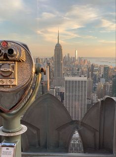 a coin operated telescope on top of a building in new york city, with the empire building in the background