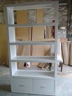 a white bookcase with drawers and shelves in the process of being built into an unfinished room