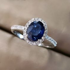 an oval shaped blue sapphire and diamond ring on a beige cloth with diamonds around it