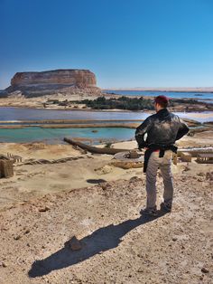 a man standing on top of a sandy beach next to the ocean with a rock formation in the background