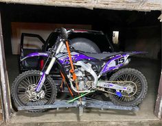 a purple dirt bike parked in a garage next to a black truck with the door open