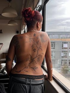 a woman with tattoos on her back standing by a window looking out at the city