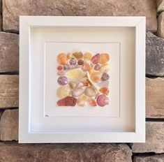 a white frame with shells in it sitting on top of a stone wall next to a brick wall