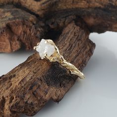 a gold ring with a white diamond sitting on top of a piece of driftwood