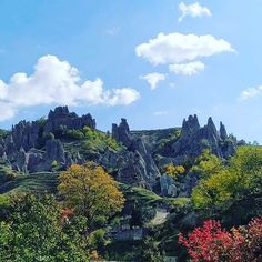 there are many trees and rocks on this mountain side with blue sky in the background