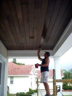 a man is painting the roof of a house with wood planks and white paint