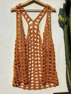 an orange crocheted tank top hanging on a white wall next to a cactus