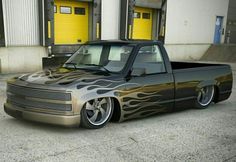 a truck with flames painted on the hood parked in front of a building and yellow doors