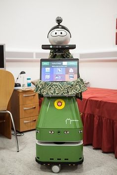 a green robot sitting on top of a bed in front of a laptop computer monitor