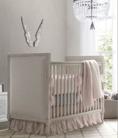 a white crib with pink bedding and a chandelier