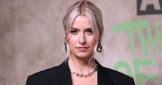 a woman with blonde hair wearing a black blazer and silver earrings is looking at the camera