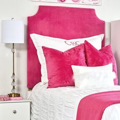 a bed with pink and white pillows on top of it next to a night stand