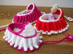 two crocheted baby shoes with a doll in the top one is pink and white